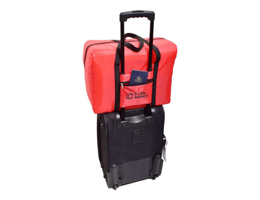 A red emergency travel bag is positioned on top of a black wheeled bag, with a passport visible in the front pocket.