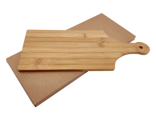 A bamboo cheese board with a handle, placed on a brown cardboard backing. It features a natural wood finish.