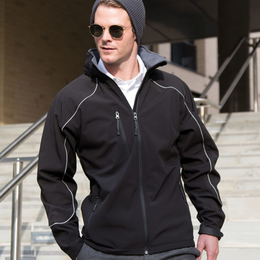 A black softshell jacket with a hood, featuring zippered pockets and a contrasting grey lining, worn by a model.