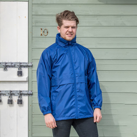 A blue windcheater jacket with a high collar and zip front, worn by a person standing against a green wooden backdrop.