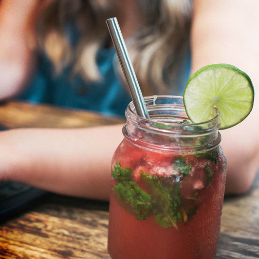 A drink featuring a stainless steel telescopic straw, garnished with a lime slice, served in a jar.