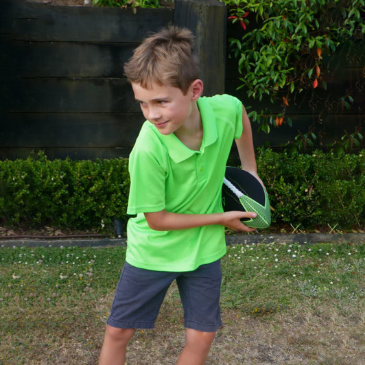 A boy wearing a bright green polo shirt and grey shorts holds a football while playing in a yard.