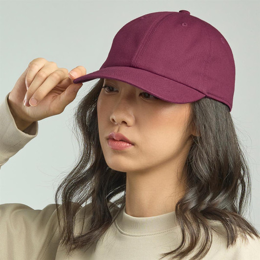 A maroon dad hat is being worn by a person with long hair, featuring a simple design and a logo.