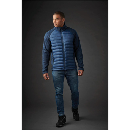 A men's hybrid jacket in navy blue, featuring a padded front and textured sleeves. The model is wearing jeans and black shoes.