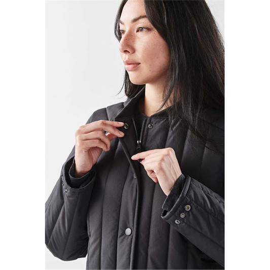 A woman in a black thermal jacket adjusts the collar, showcasing its sleek design and button details.