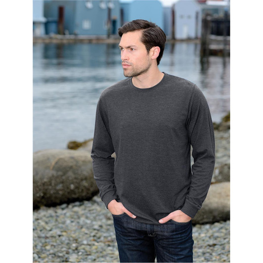A man wearing a charcoal long-sleeve t-shirt, standing by a waterfront with colourful buildings in the background.