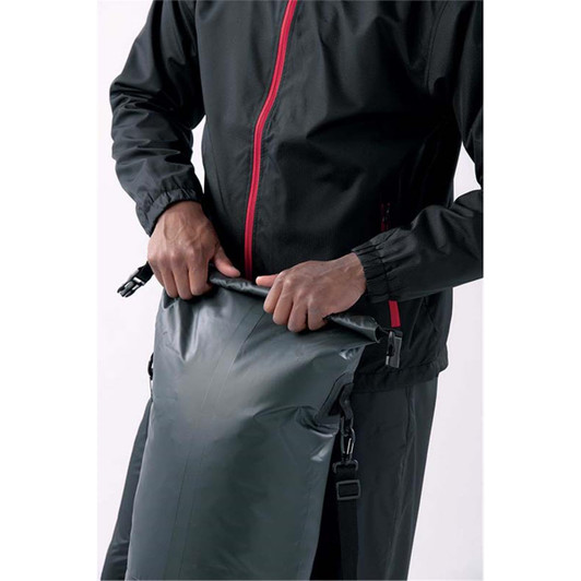 A person is holding the roll-top opening of a grey Nautilus 25 Backpack, wearing a black jacket.