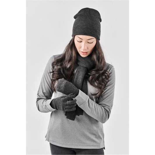A woman wearing a black knit beanie, matching scarf, and gloves, styled with a grey long-sleeve top.