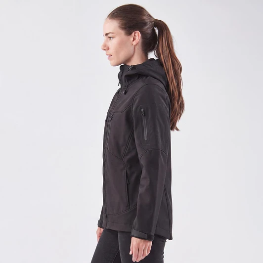 A women's softshell jacket in black, featuring a hood and zippered pockets, displayed on a model from the side.
