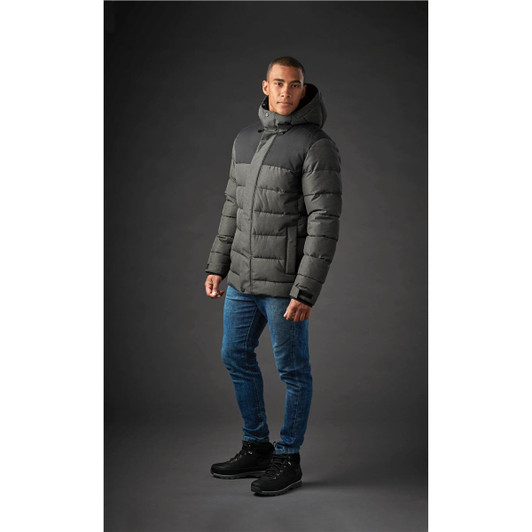 A men's parka in dark grey with a hood, featuring a quilted design and worn over denim jeans and boots.