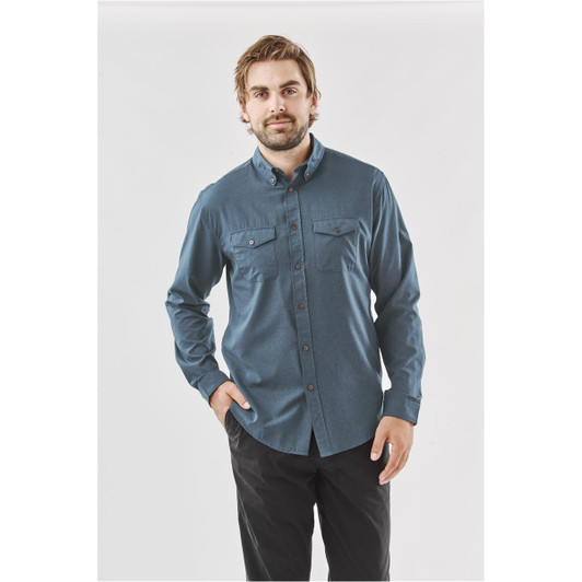 A model wearing a men's long-sleeve shirt in blue, featuring two chest pockets and a button-down collar.