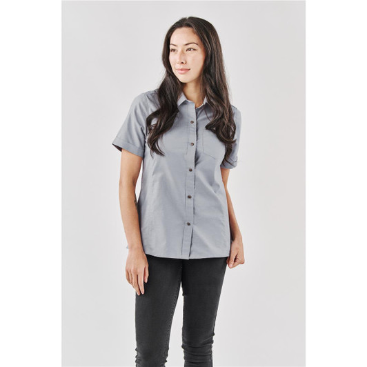 A short-sleeved, button-up shirt in grey, modelled by a woman, featuring a logo on the chest area.