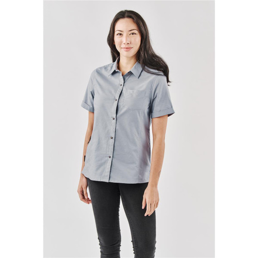 A woman wearing a light grey button-up shirt with a collar, featuring a logo on the chest pocket.