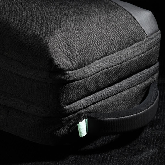 A black backpack with a textured exterior and a mint green zipper pull, featuring a side handle.