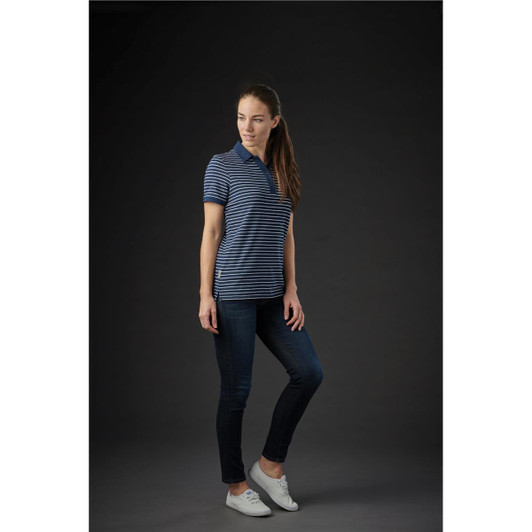 A woman wearing a navy and white striped polo shirt with a logo, paired with jeans and white shoes.