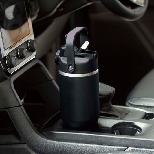 A drink bottle with a black exterior and a handle, placed in a vehicle's cup holder. It has a sleek design and a logo.