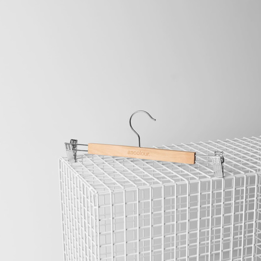 A wooden clip hanger in natural colour with metal clips, displayed on a white wire grid.