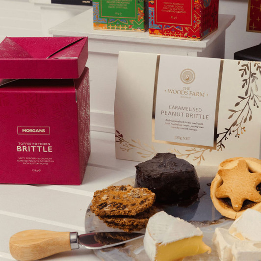 A pink gift box beside a plate with various treats, including caramelised peanut brittle, biscuits, and sweets.