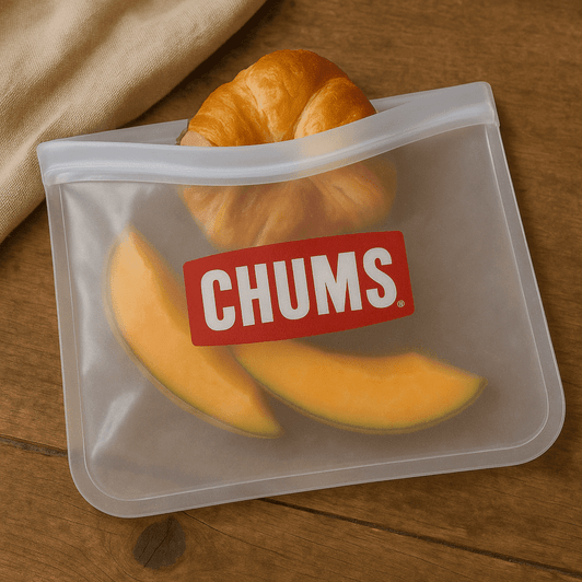A transparent PEVA reusable food storage bag with a croissant and slices of cantaloupe inside, featuring a logo.