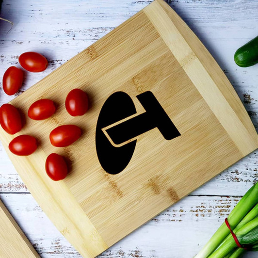 A bamboo cutting board displaying a logo, with cherry tomatoes and chopped spring onions alongside it.