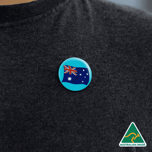 A 25mm button badge featuring the Australian flag, displayed on a dark clothing item, with a logo in the corner.
