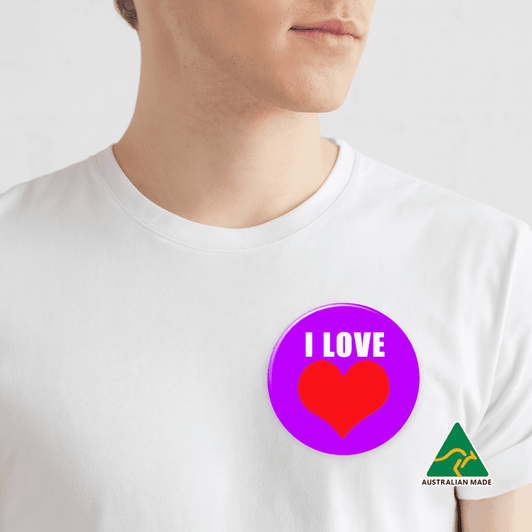 A purple button badge featuring a red heart design, attached to a white shirt on a plain background.