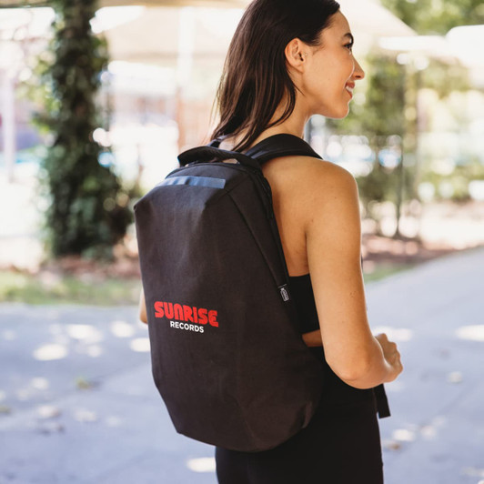 A black backpack with a logo, worn by a woman outdoors. The design is sleek and modern.
