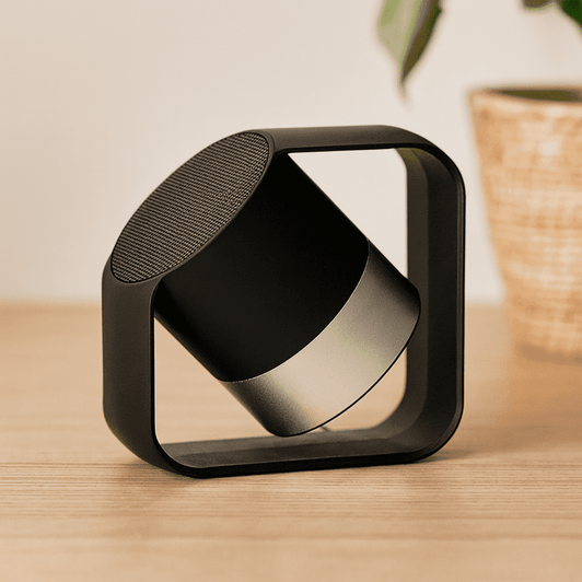 A black and silver wireless speaker on a wooden surface, featuring a modern geometric design and a visible logo.