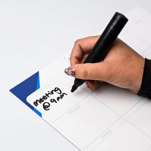 A hand holding a black marker writes on a white magnetic whiteboard with a blue corner.