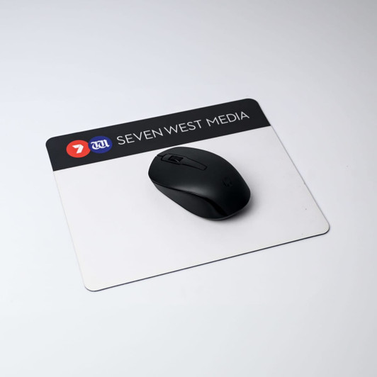 A black mouse sits on a rectangular, white mouse mat with a logo at the top. The mat has a natural rubber base.
