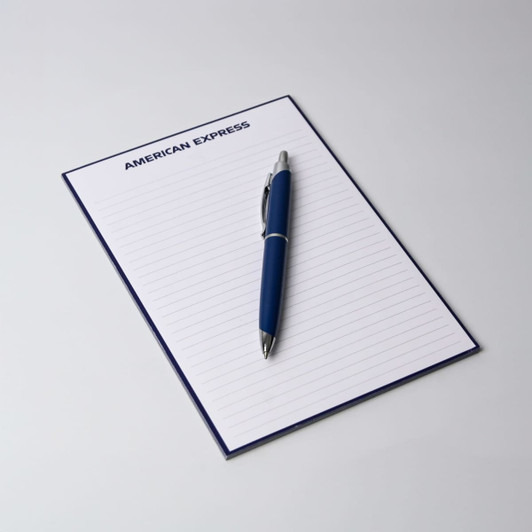 A5 notepad with 50 lined leaves, featuring a blue cover and a silver pen placed on top. It has a logo at the top.