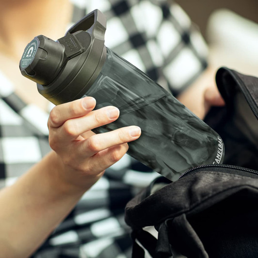 A drink bottle with a black lid and a transparent body being taken from a black bag. Features a logo.