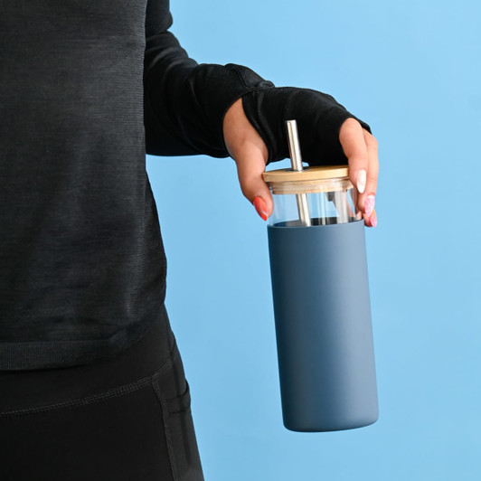 A drink bottle with a blue exterior, clear top, and bamboo lid, featuring a straw and held by a person.