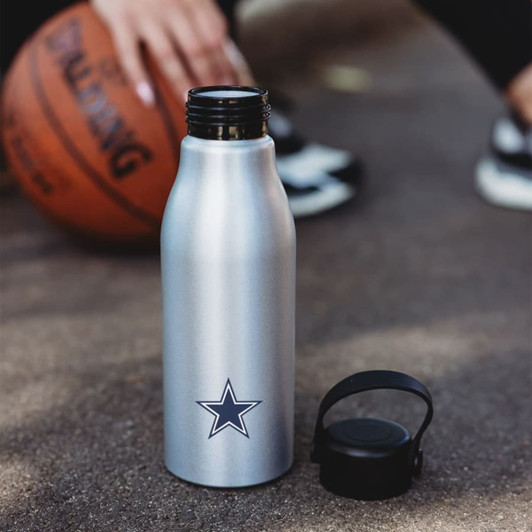A drink bottle in silver with a black lid and a star logo, set on a textured surface beside a basketball.