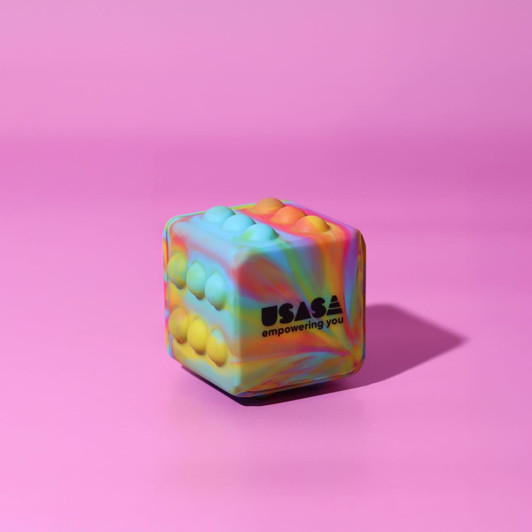 A colourful, rainbow-patterned cube featuring textured bumps, set against a pink background, with a logo.