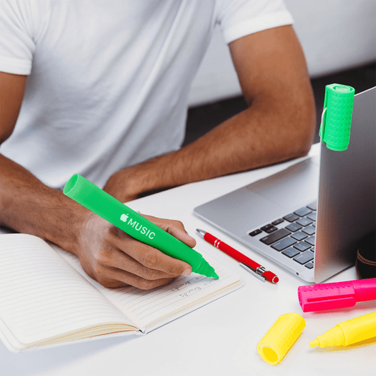 A collection of highlighters in bright colours, including green, pink, and yellow, alongside a notebook and laptop.