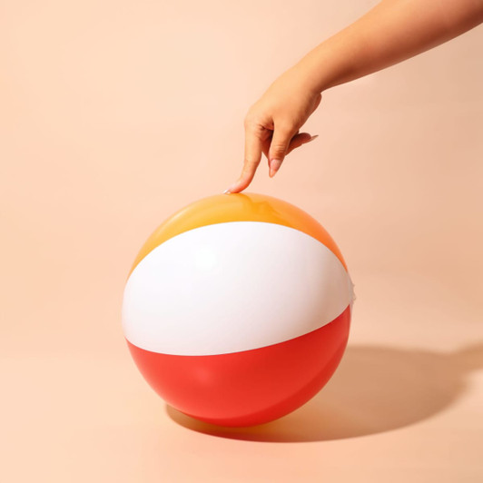 A colourful beach ball featuring orange, white, and red panels, with a hand positioned on top.