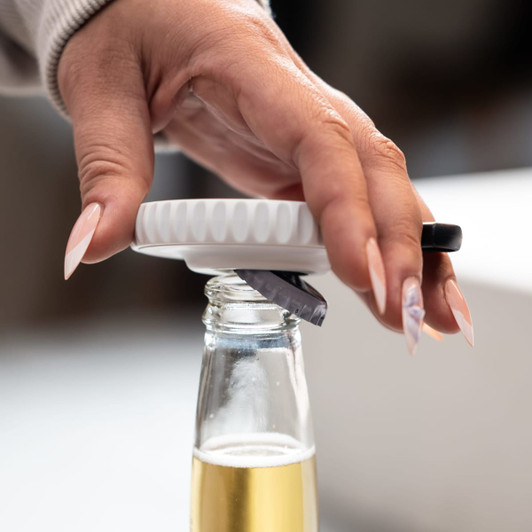 A drink bottle with a white spinner cap and black bottle opener. The cap is being held by a hand with long nails.