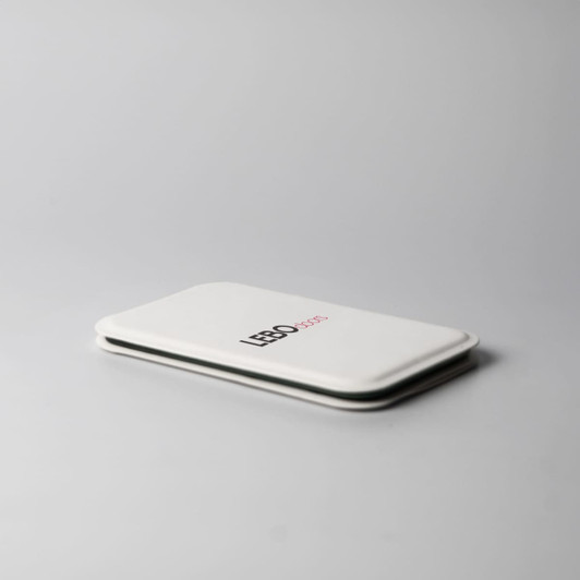 A white pocket mirror with a sleek design and a logo on the front, resting on a light grey surface.