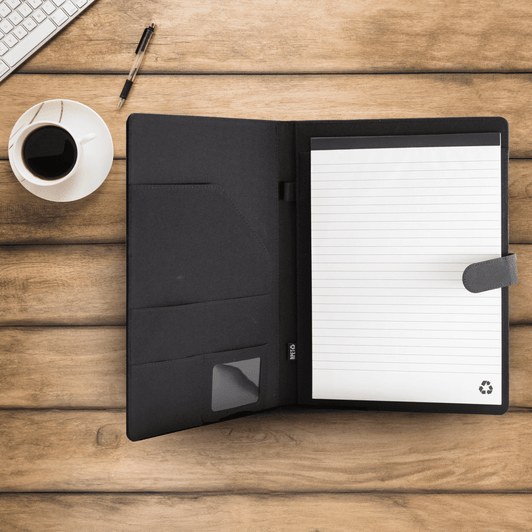 A black RPET portfolio opened to reveal lined paper and pockets, set on a wooden surface with a coffee cup and pen.