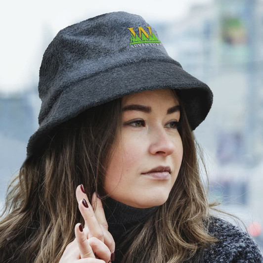 A grey terry towelling bucket hat with a logo, worn by a woman with long hair in an outdoor setting.