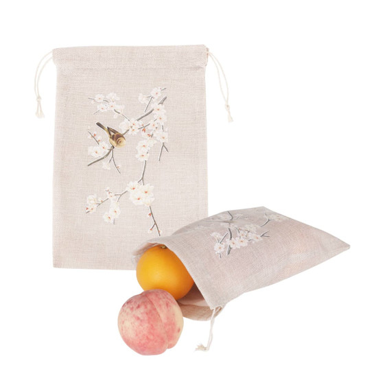 A small beige jute produce bag with floral designs, containing an orange and a pink apple.