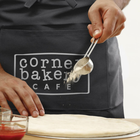 A dark grey waist apron features a logo, with a person using a scoop above a pizza dough.