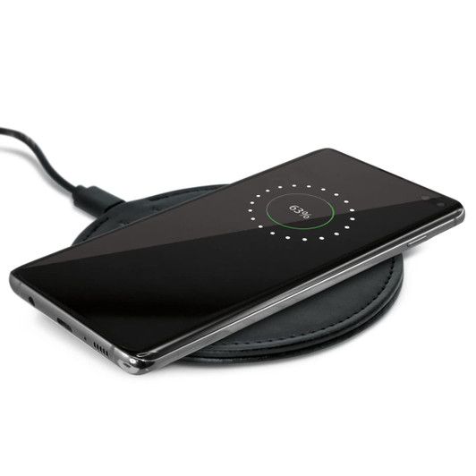 A wireless charger with a smartphone placed on top, displaying a charging indicator on the screen.