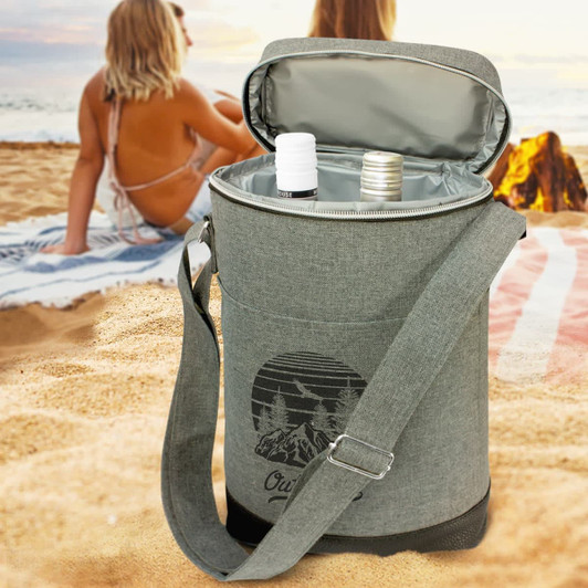 A grey wine cooler bag with a shoulder strap, open and containing two bottles, set on a sandy beach.
