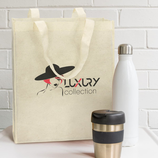 A natural look tote bag in cream colour, accompanied by a stainless steel drink bottle and a metal coffee cup.