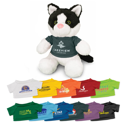 A soft black and white cat plush toy wearing a green T-shirt with a logo. Multiple other T-shirts in various colours are arranged below.
