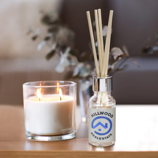 A glass scented diffuser bottle with a silver cap and wooden reeds, alongside a lit glass candle.