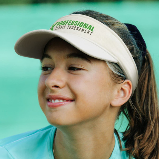 A beige sports mesh visor with a logo, worn by a young girl, set against a green background.