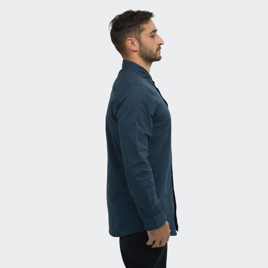 A side view of a man wearing a dark blue TRENDSWEAR button-up poplin shirt. The shirt has a collar and long sleeves.